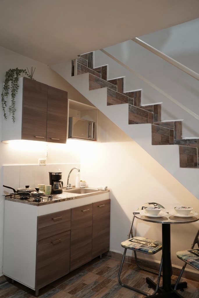Cocina tipo loft bajo escalera con mesa para dos y equipamiento completo
