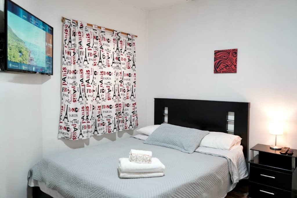 Dormitorio tendido con almohadas, televisión y cortinas